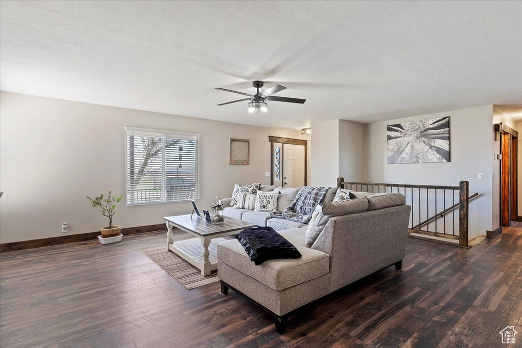 Living area featuring a textured ceiling, dark wood-style flooring, ceiling fan, and baseboards