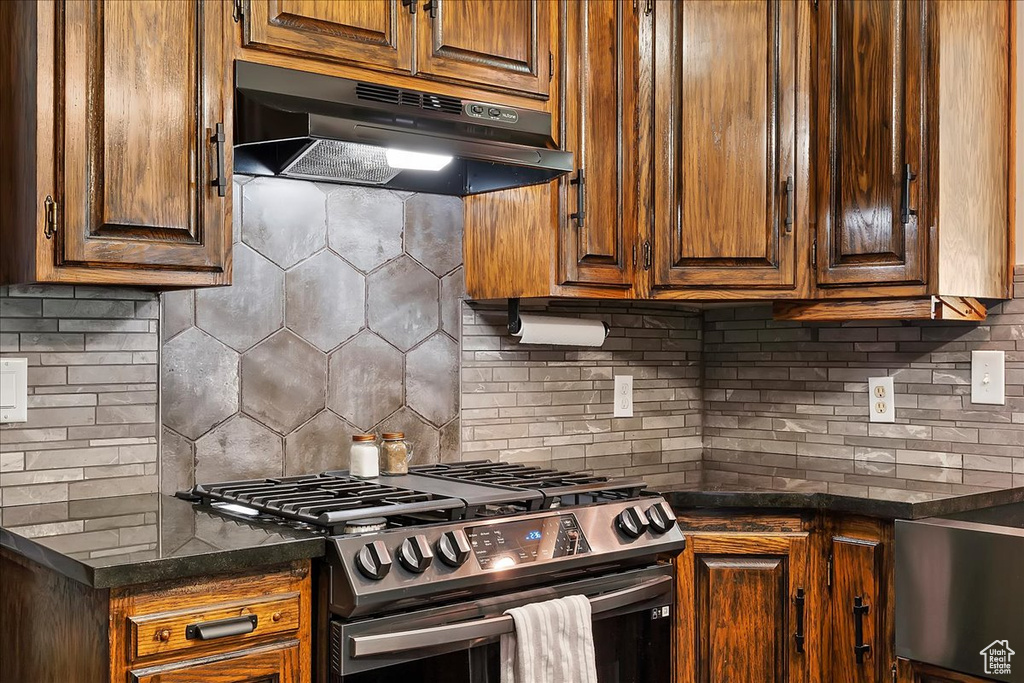 Kitchen featuring under cabinet range hood, backsplash, and stainless steel range with gas cooktop
