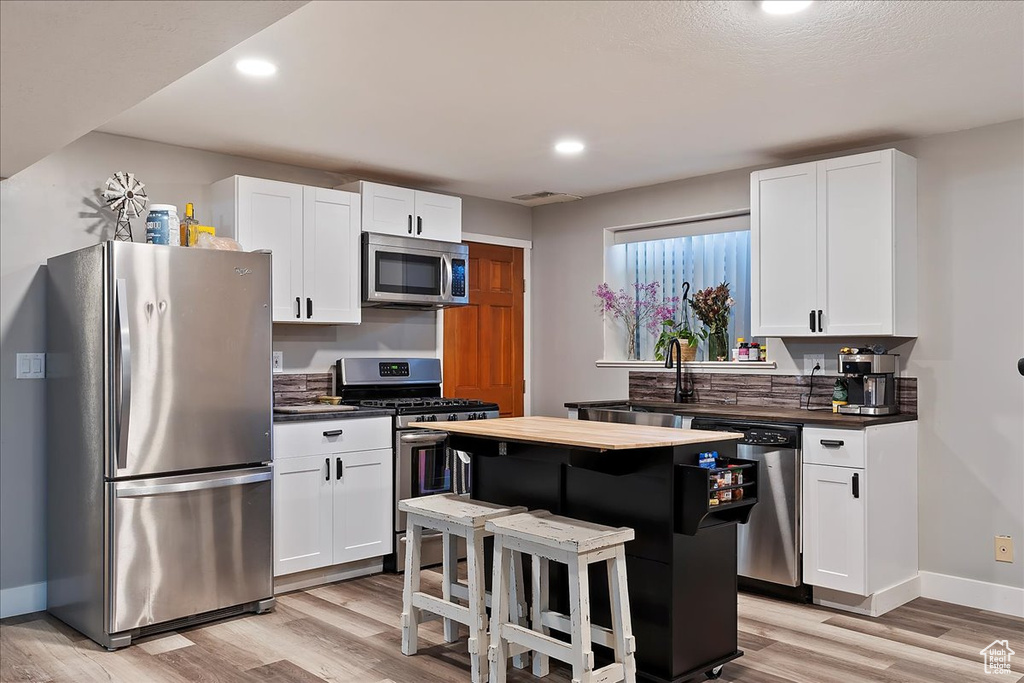 Kitchen featuring a sink, white cabinetry, appliances with stainless steel finishes, light wood-style flooring, and baseboards