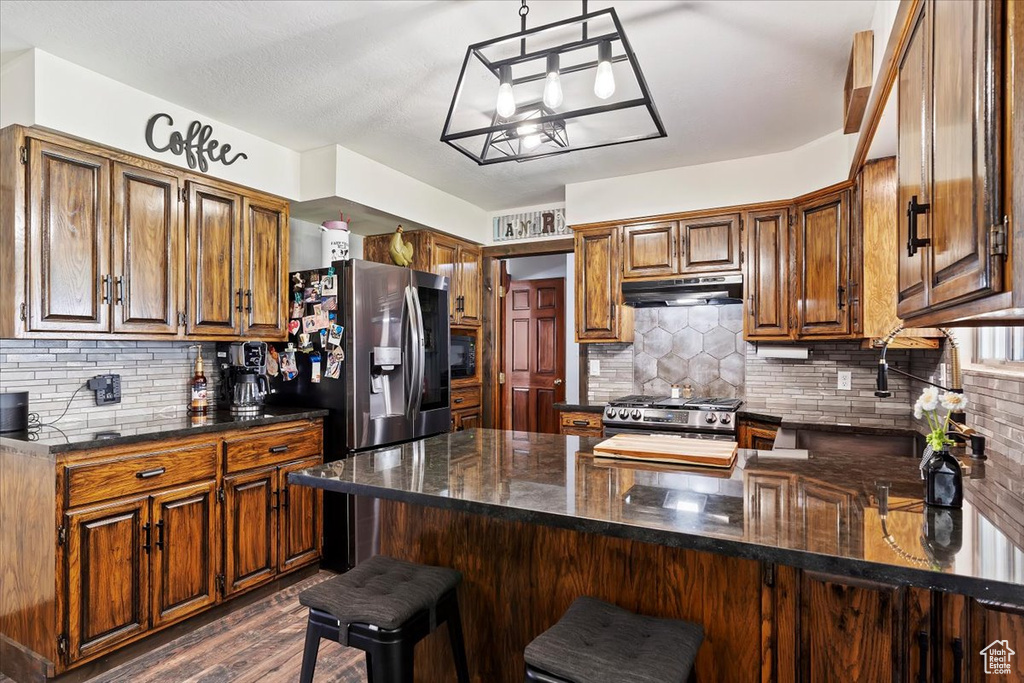 Kitchen featuring brown cabinets, under cabinet range hood, appliances with stainless steel finishes, and a peninsula