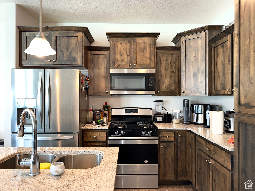Kitchen with dark brown cabinetry, a textured ceiling, light stone countertops, and appliances with stainless steel finishes