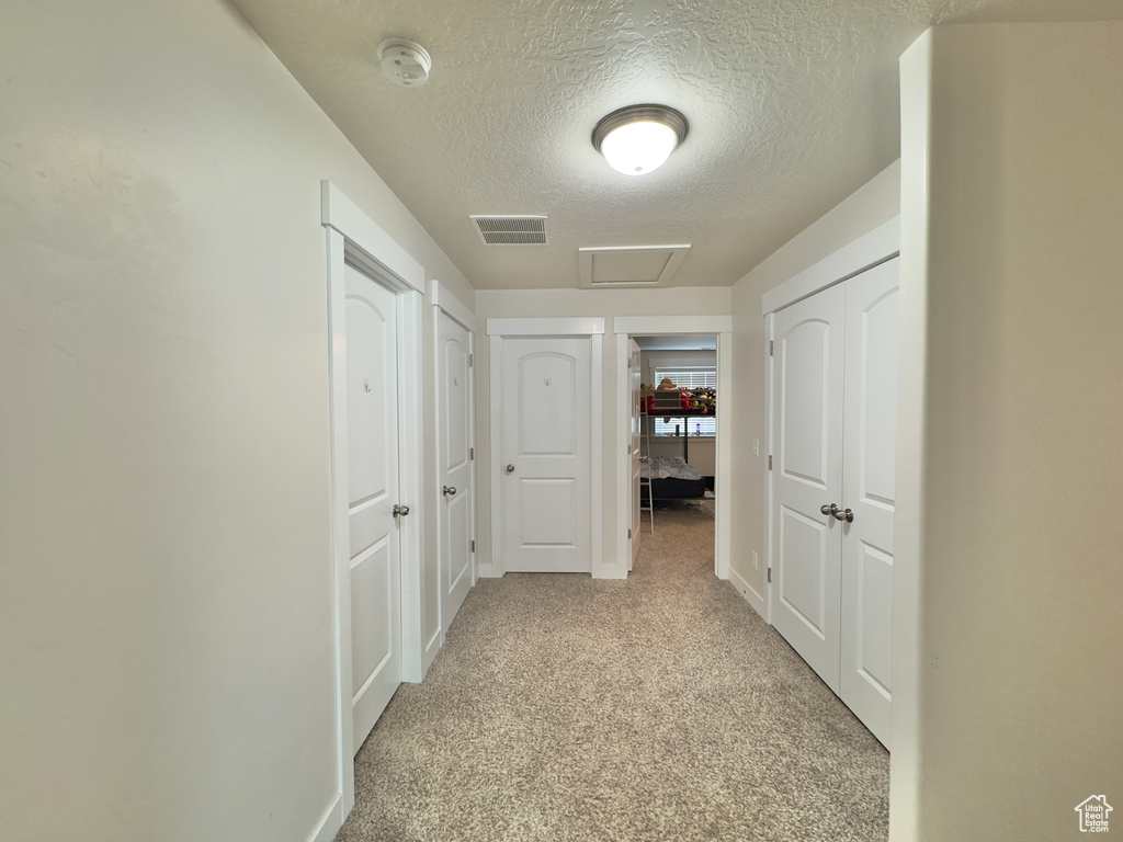 Hall featuring a textured ceiling, visible vents, baseboards, attic access, and light colored carpet