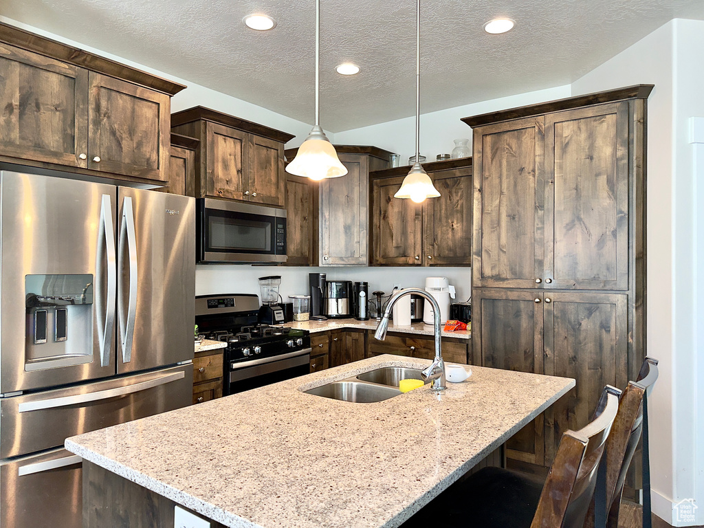 Kitchen with a sink, light stone counters, dark brown cabinets, and appliances with stainless steel finishes