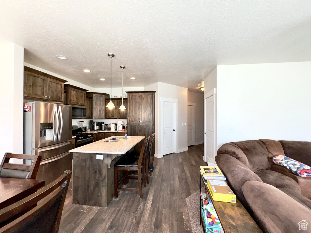 Kitchen with a kitchen breakfast bar, open floor plan, a sink, dark brown cabinets, and appliances with stainless steel finishes