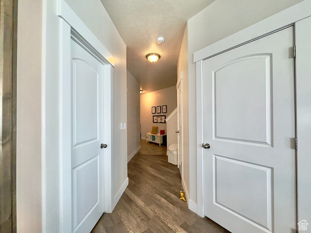 Hall featuring baseboards, dark wood-style flooring, and a textured ceiling