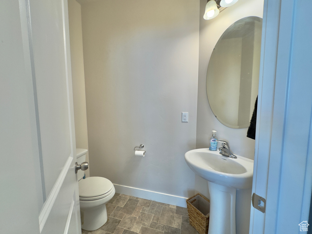 Half bathroom featuring toilet, stone finish flooring, and baseboards