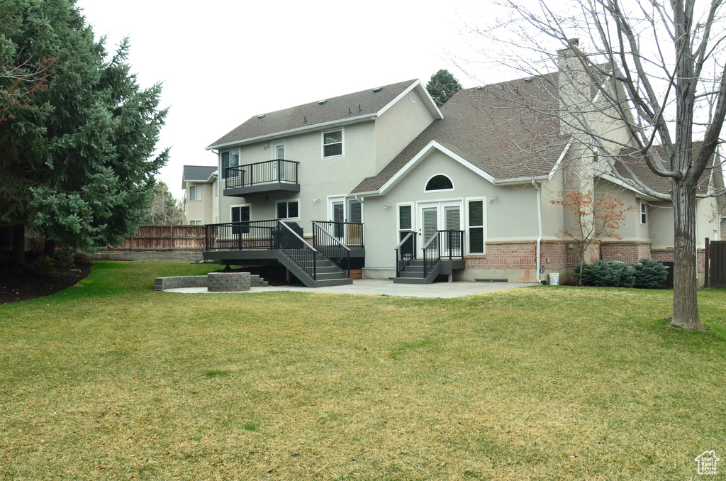 Rear view of house featuring a balcony, stucco siding, fence, and a lawn