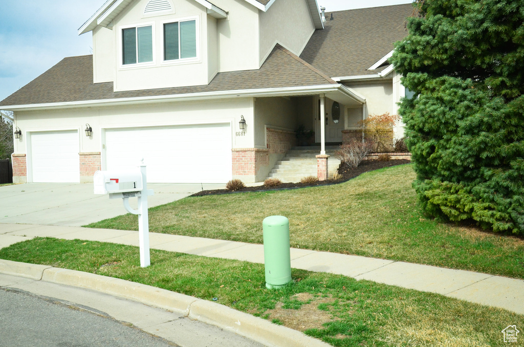 View of front facade with driveway, stucco siding, an attached garage, brick siding, and a front lawn