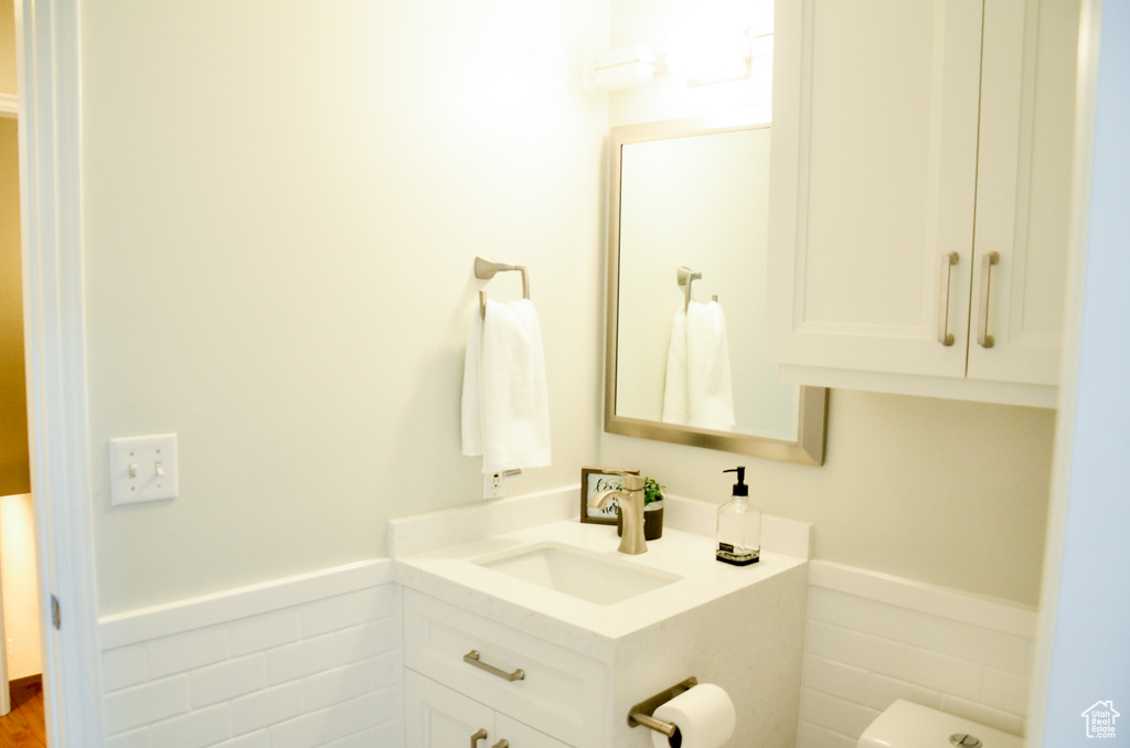 Bathroom with tile walls, a wainscoted wall, toilet, and vanity