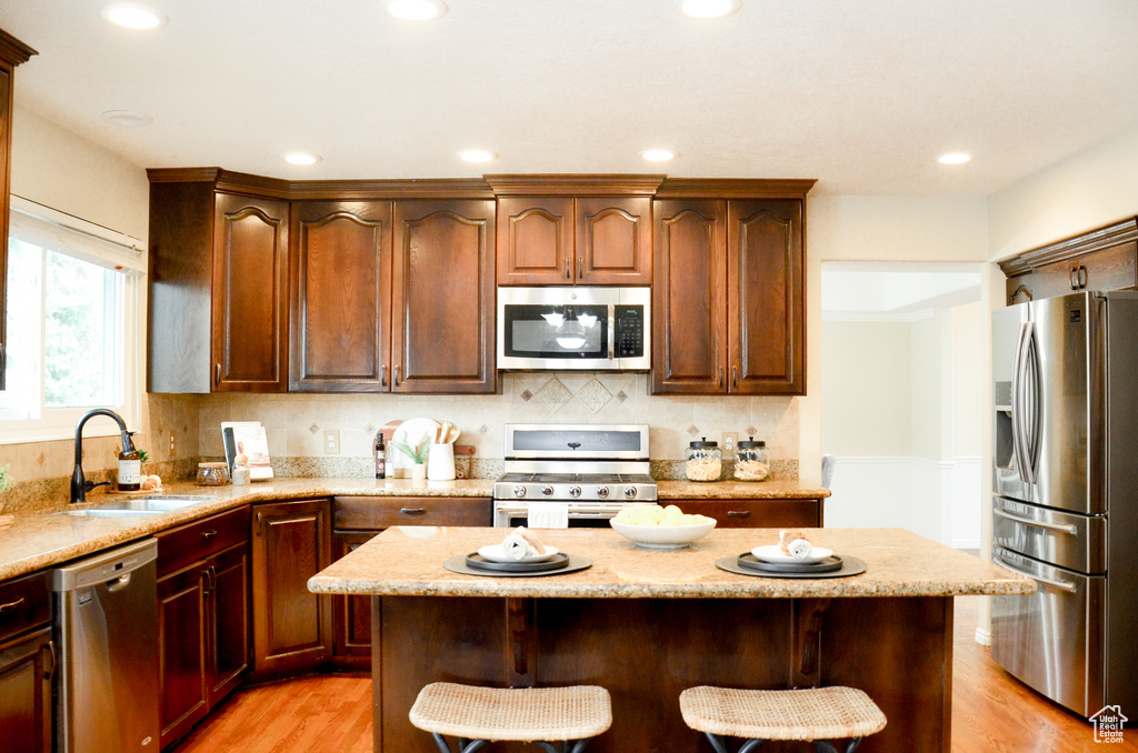 Kitchen featuring light stone countertops, a breakfast bar area, decorative backsplash, stainless steel appliances, and a sink