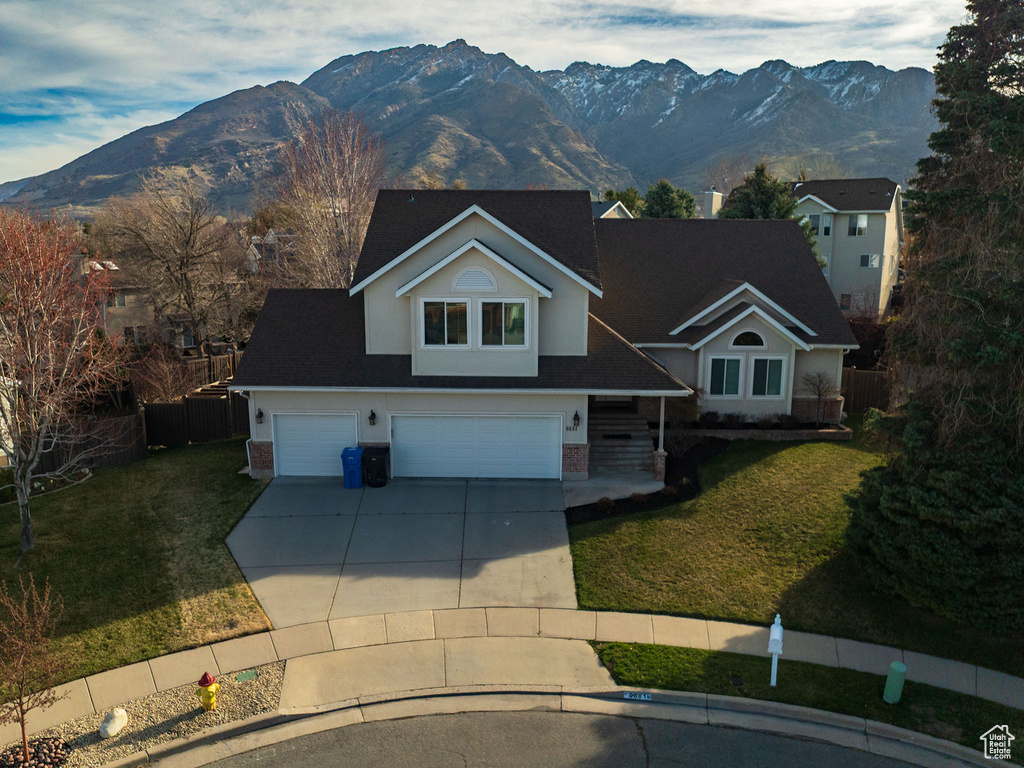 Traditional home with fence, a front lawn, an attached garage, a mountain view, and concrete driveway
