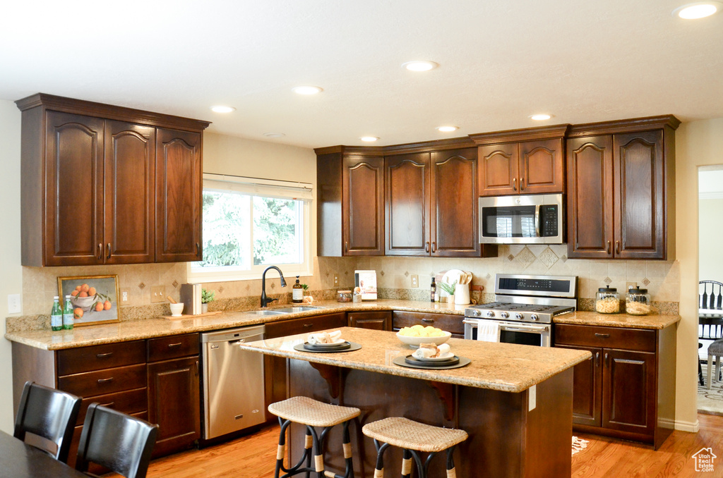 Kitchen featuring a breakfast bar area, stainless steel appliances, backsplash, a sink, and light wood-style floors