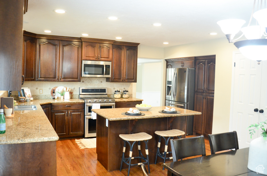Kitchen featuring light wood finished floors, light stone countertops, a breakfast bar, a center island, and stainless steel appliances