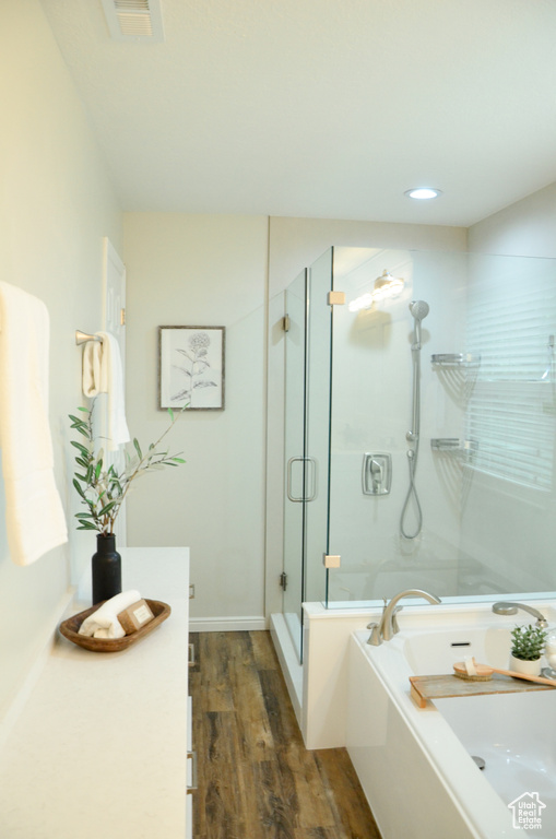 Bathroom featuring a bath, visible vents, wood finished floors, vanity, and a stall shower