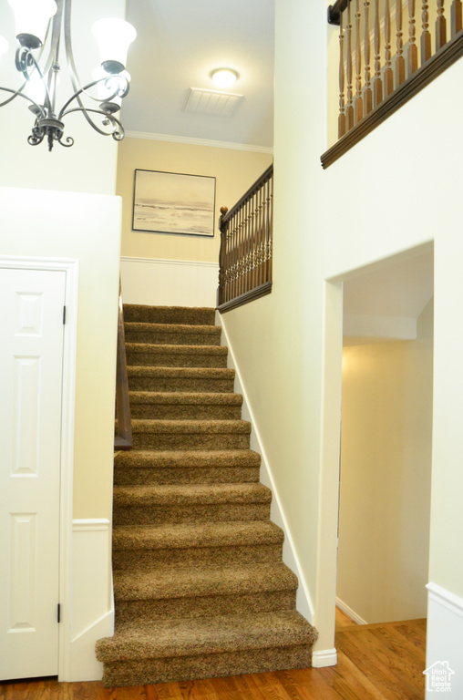 Stairway featuring wood finished floors, crown molding, a chandelier, and visible vents