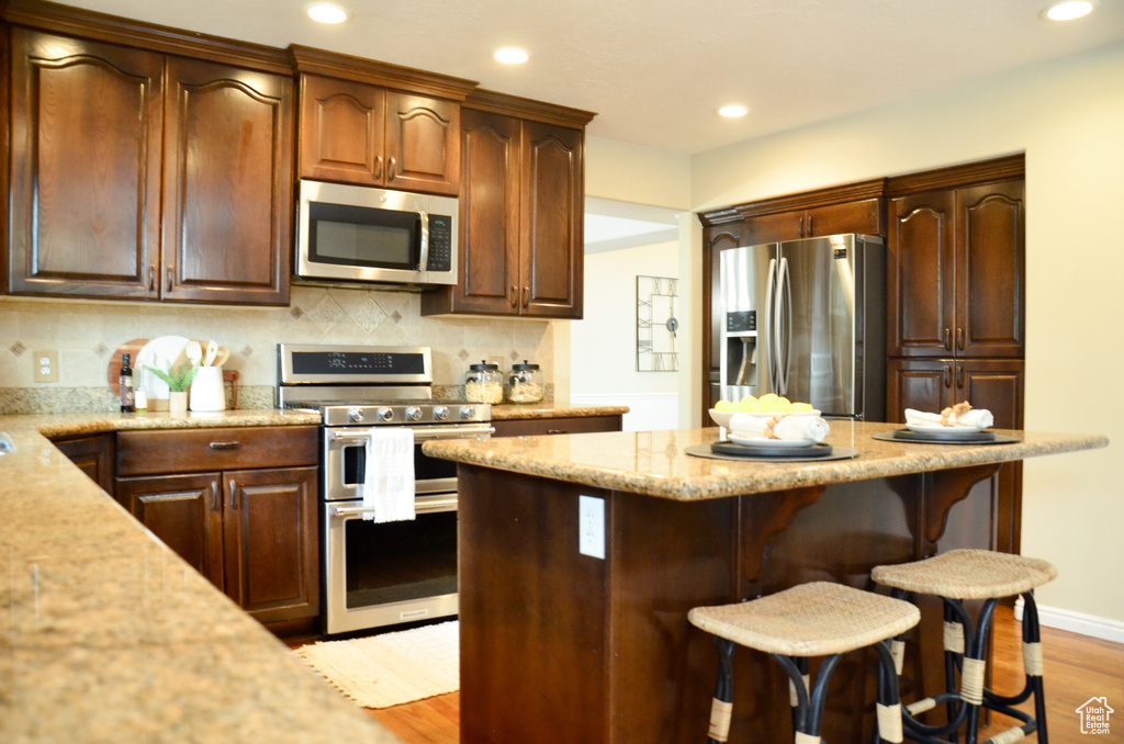 Kitchen with tasteful backsplash, stainless steel appliances, a breakfast bar, light wood-style floors, and light stone counters