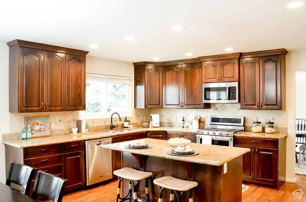 Kitchen with light wood-type flooring, appliances with stainless steel finishes, decorative backsplash, and a sink