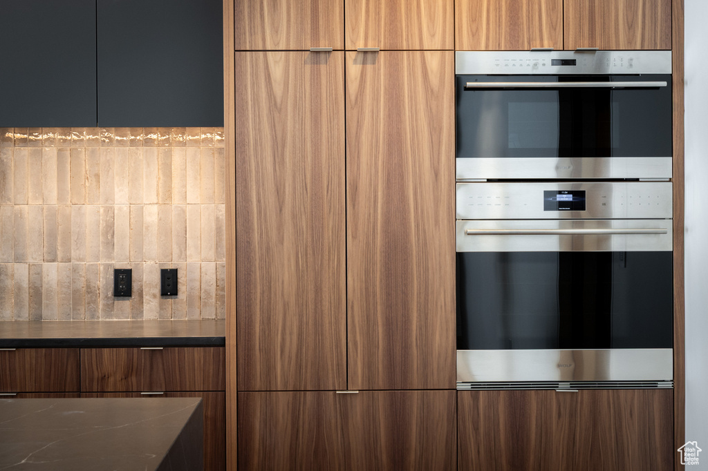 Kitchen featuring modern cabinets, brown cabinets, dark countertops, and stainless steel double oven