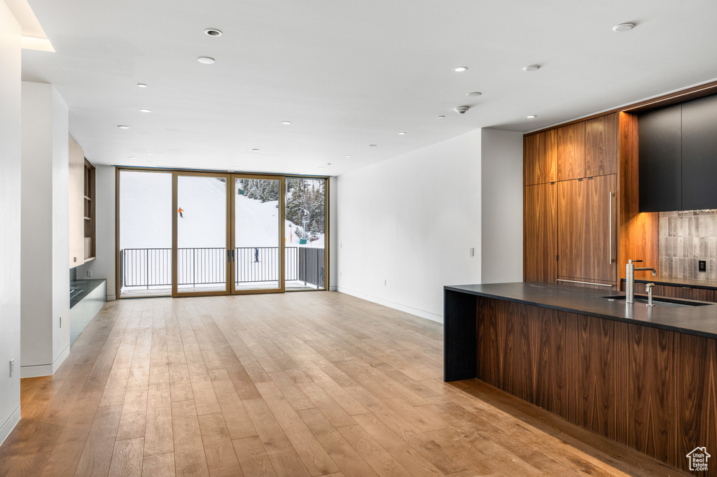 Kitchen with floor to ceiling windows, a sink, dark countertops, light wood finished floors, and modern cabinets