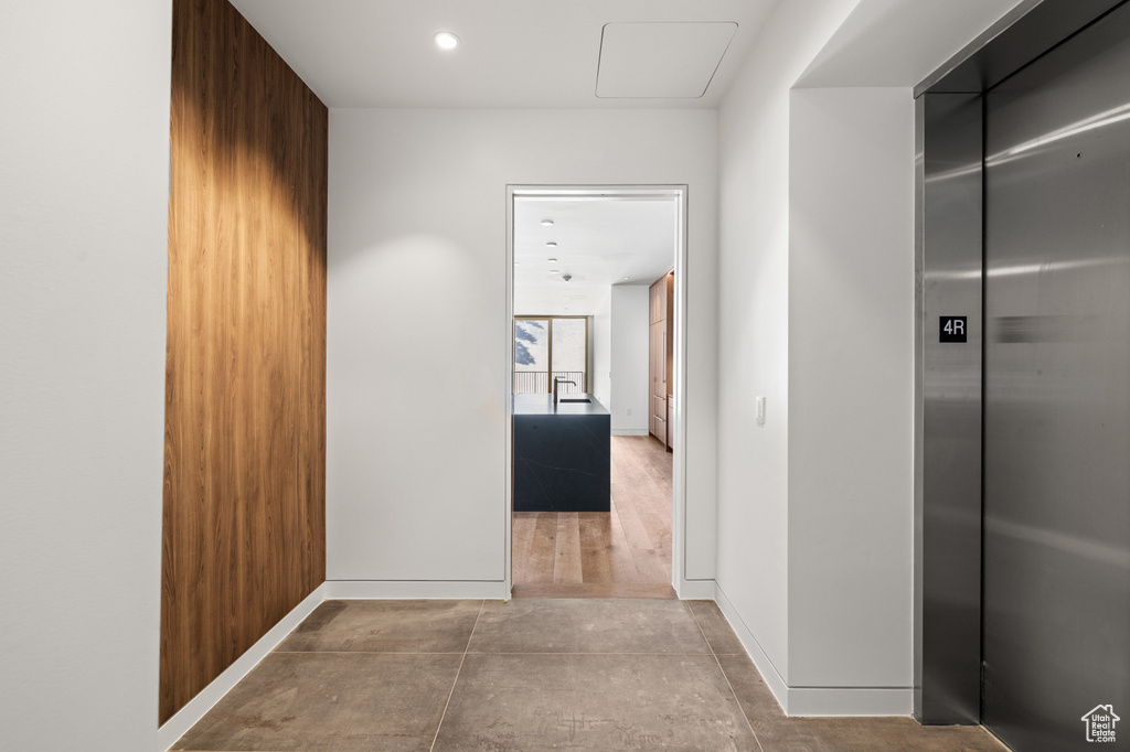 Hallway featuring elevator, concrete floors, baseboards, and recessed lighting