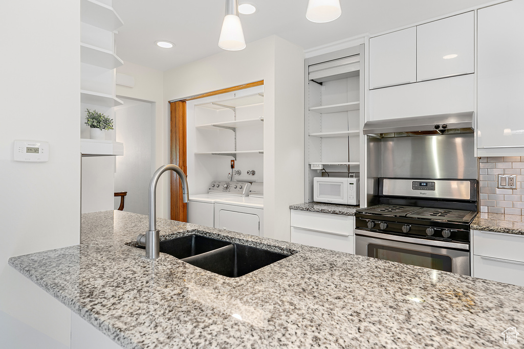 Kitchen with open shelves, a sink, gas range, white microwave, and washing machine and dryer