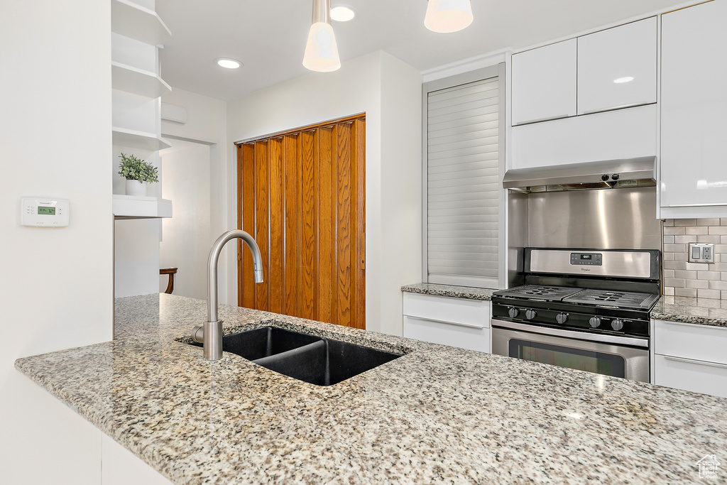Kitchen featuring exhaust hood, tasteful backsplash, open shelves, stainless steel gas stove, and a sink