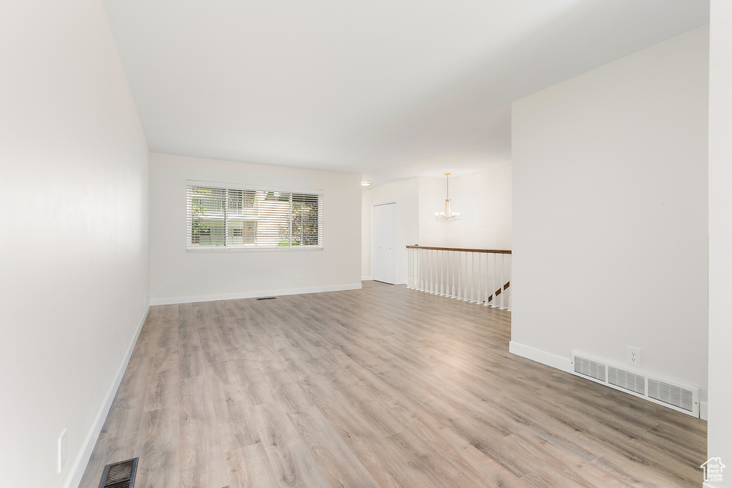 Empty room with light wood-style floors, a chandelier, and visible vents