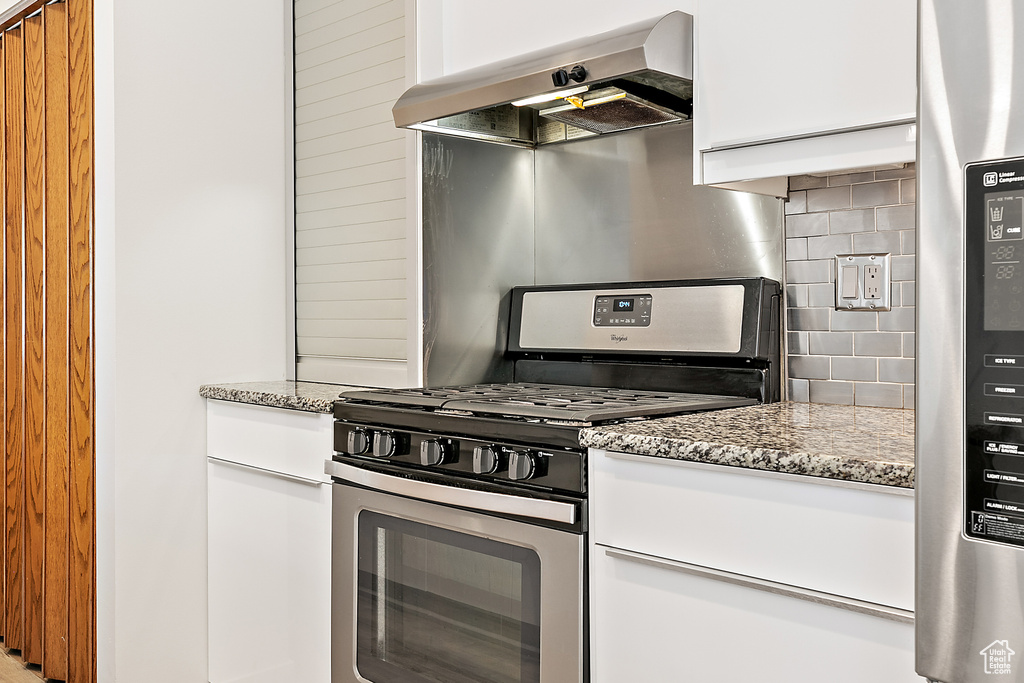 Kitchen with wall chimney exhaust hood, white cabinets, light stone counters, appliances with stainless steel finishes, and backsplash
