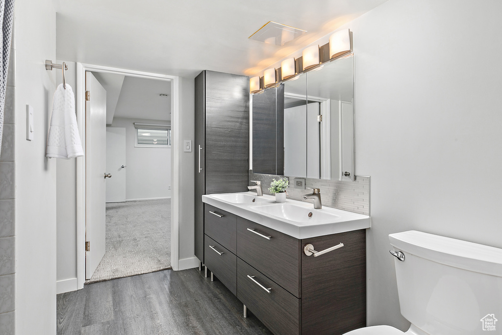 Bathroom with toilet, decorative backsplash, a sink, and wood finished floors