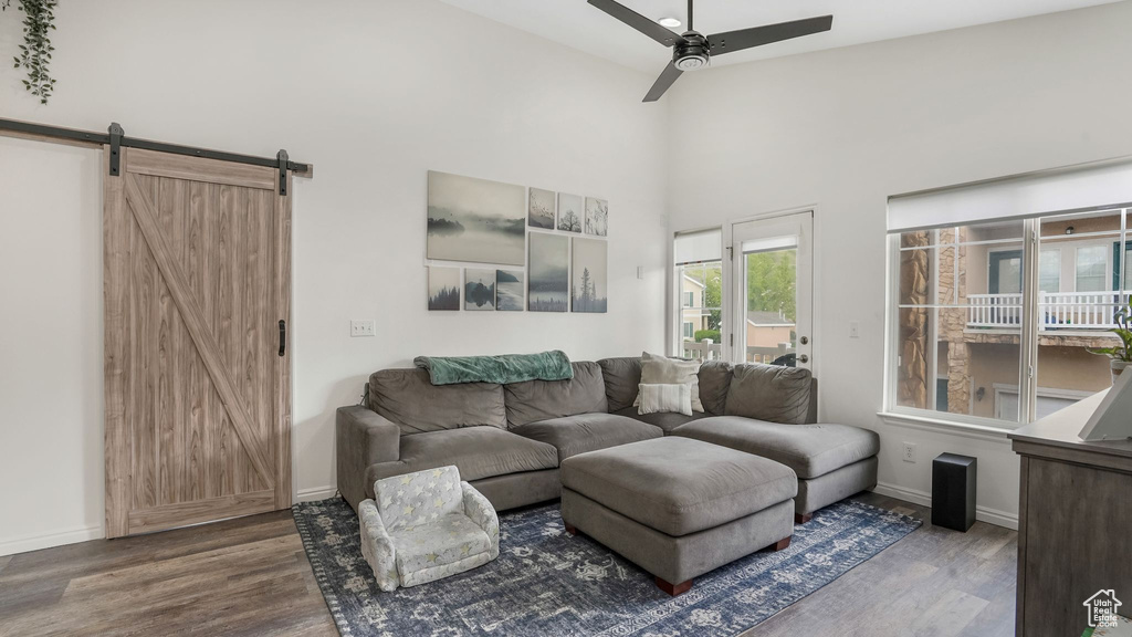Living room featuring a barn door, wood finished floors, a ceiling fan, baseboards, and a towering ceiling