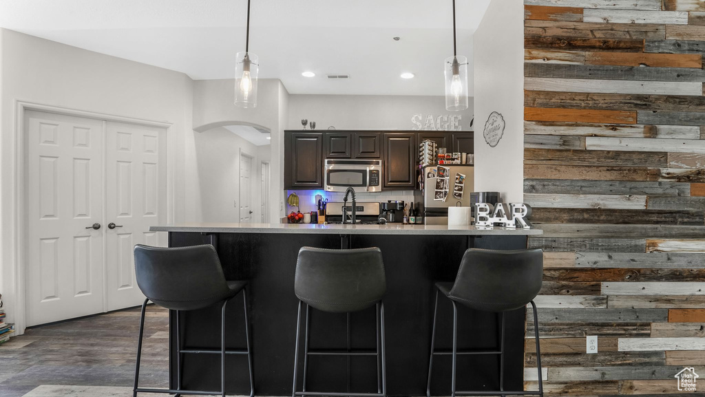 Kitchen featuring stainless steel appliances, a kitchen bar, arched walkways, light countertops, and decorative light fixtures