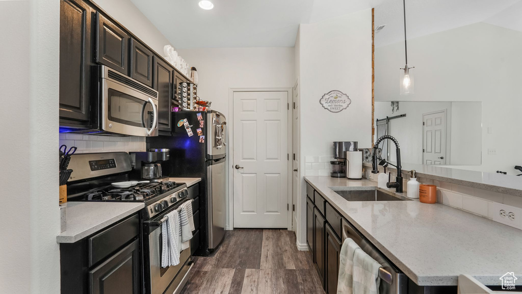 Kitchen with stainless steel appliances, a sink, dark wood-style flooring, light stone countertops, and a peninsula