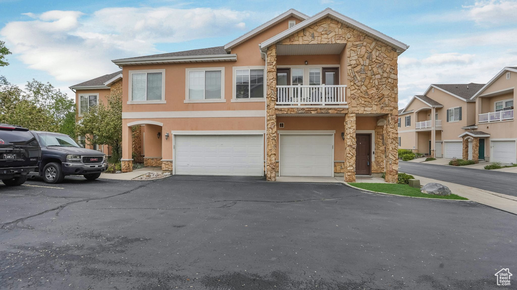View of front of property with stone siding, a garage, stucco siding, driveway, and a balcony
