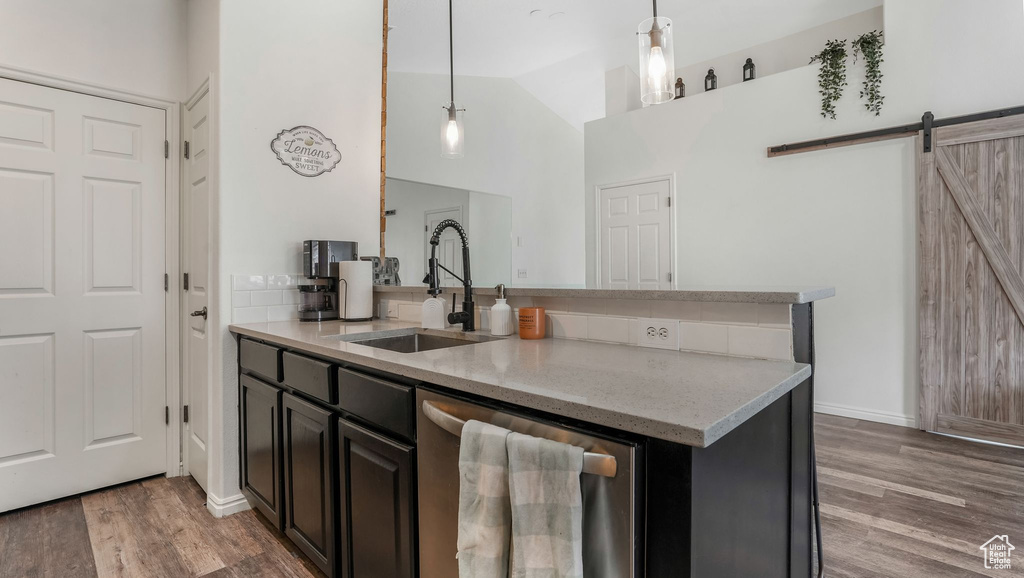 Kitchen with dishwasher, a sink, a barn door, light wood finished floors, and light stone countertops