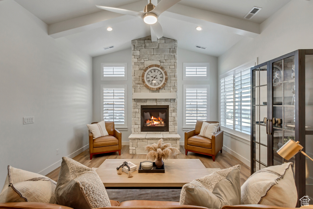 Living room featuring a stone fireplace, ceiling fan, visible vents, and wood finished floors