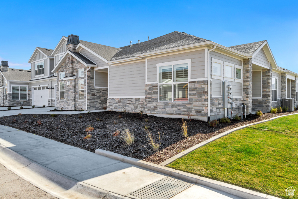 View of side of property featuring stone siding, central AC unit, a yard, and a shingled roof