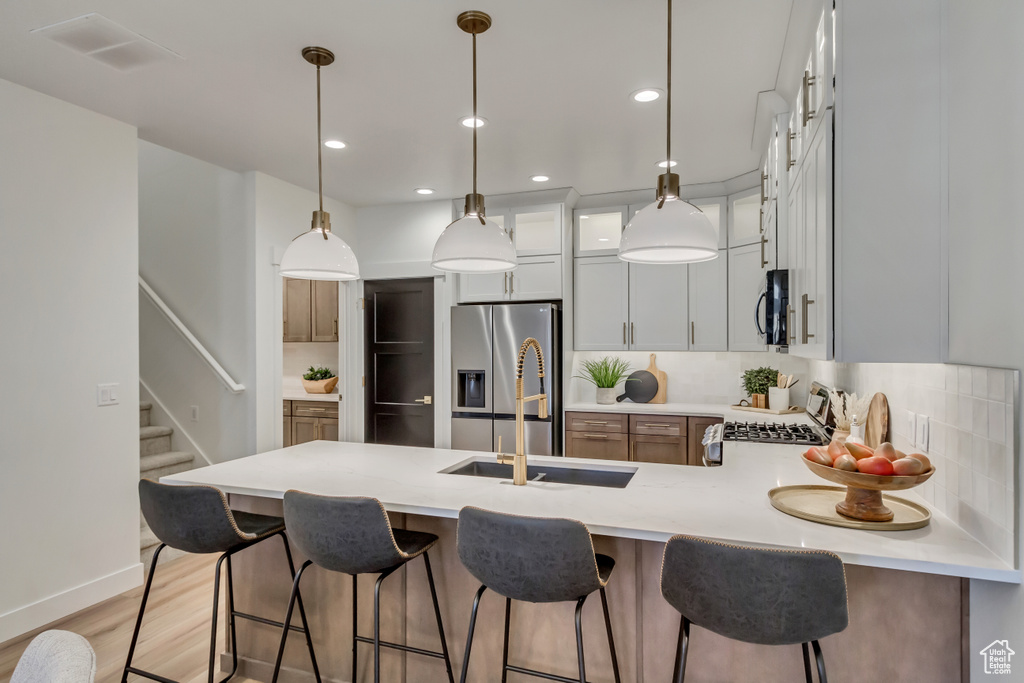 Kitchen with light countertops, a peninsula, stainless steel appliances, light wood-style floors, and backsplash