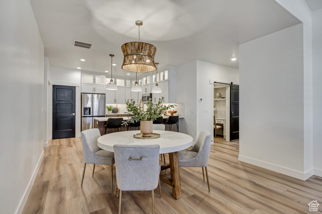Dining space with a barn door, baseboards, visible vents, light wood-style floors, and recessed lighting