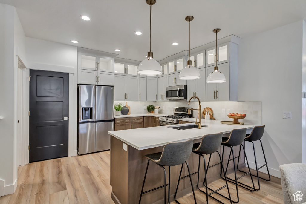 Kitchen featuring light countertops, a sink, appliances with stainless steel finishes, a peninsula, and decorative backsplash