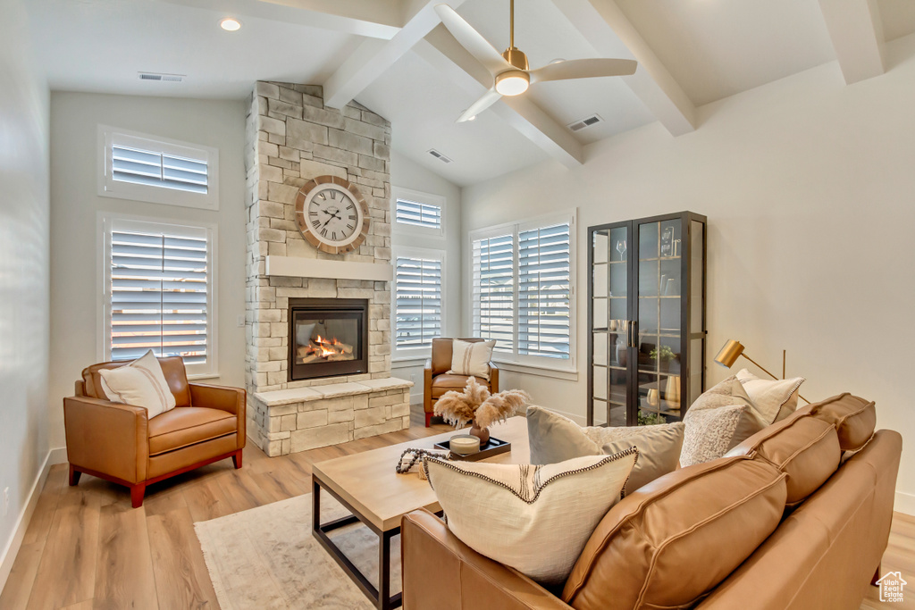 Living room featuring lofted ceiling with beams, wood finished floors, a stone fireplace, and visible vents