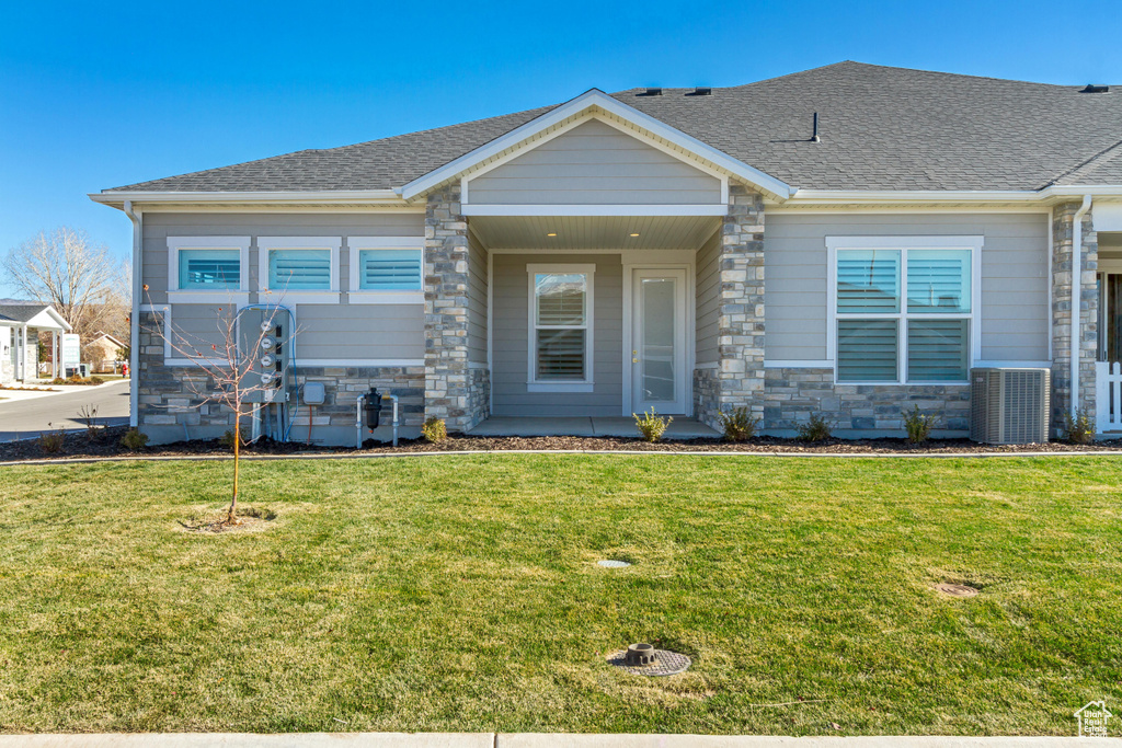 View of front of property featuring stone siding, a front yard, central AC unit, and a shingled roof