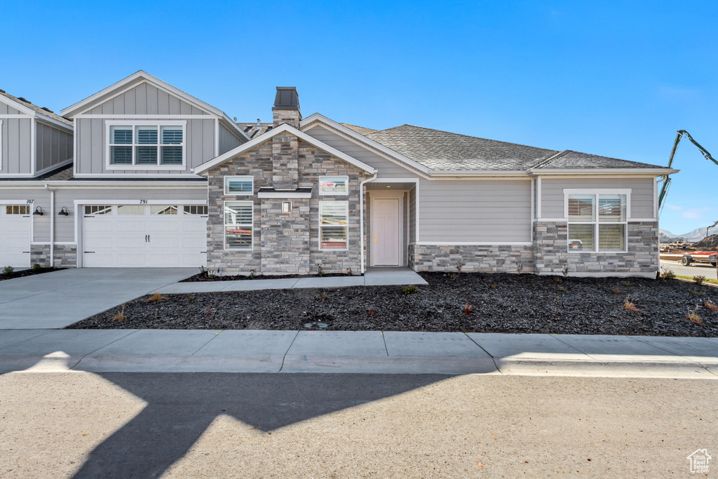 Craftsman-style house with stone siding, a chimney, a garage, board and batten siding, and driveway