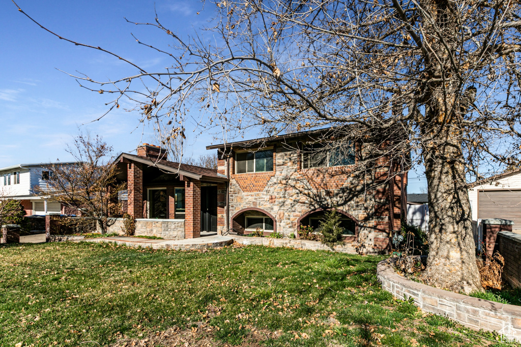View of front facade featuring stone siding, a chimney, a garage, brick siding, and a front lawn