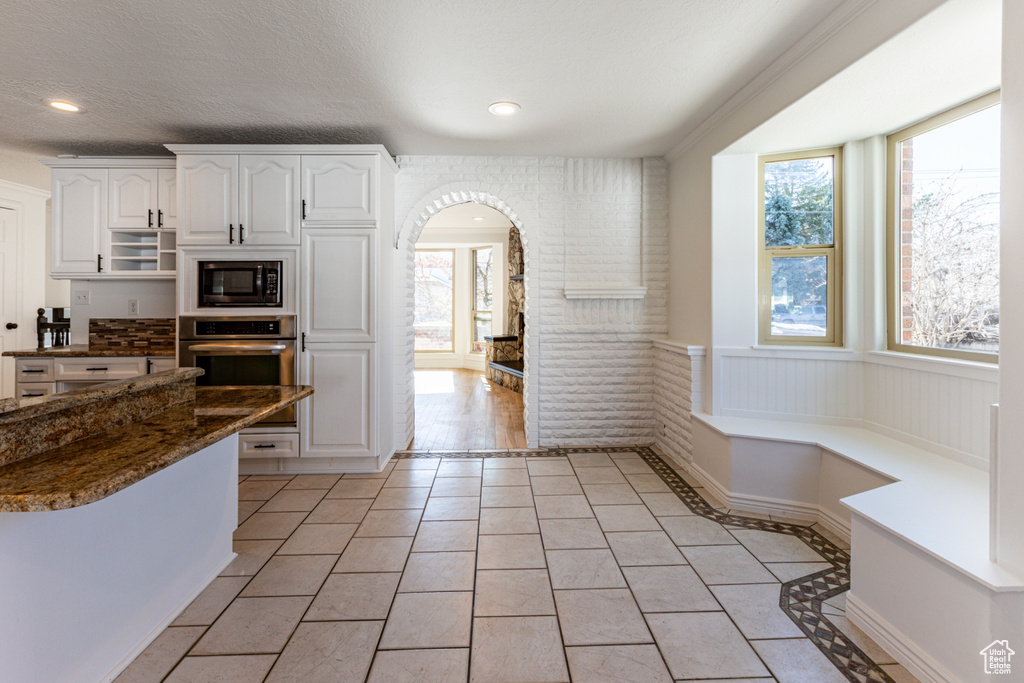 Kitchen with stainless steel oven, arched walkways, black microwave, a wealth of natural light, and light tile patterned floors
