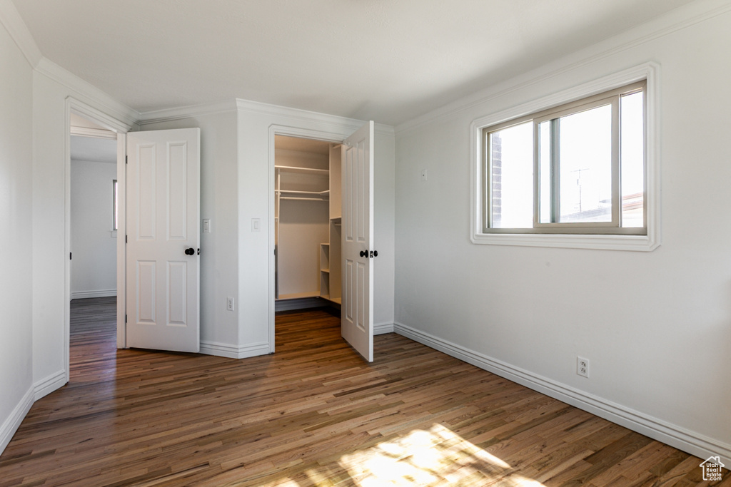 Unfurnished bedroom featuring crown molding, baseboards, a closet, and wood finished floors