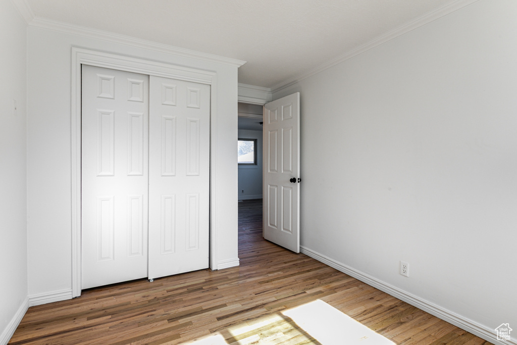 Unfurnished bedroom with baseboards, wood finished floors, a closet, and crown molding