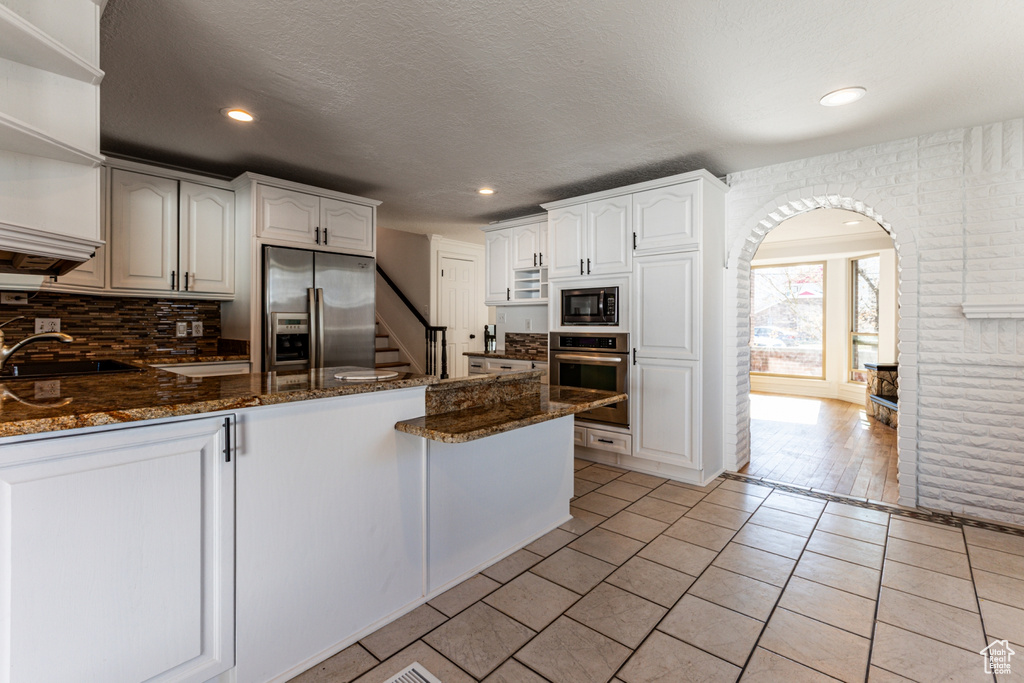 Kitchen featuring a sink, open shelves, appliances with stainless steel finishes, a peninsula, and dark stone counters