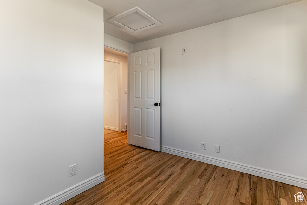 Unfurnished room featuring baseboards, wood finished floors, and attic access