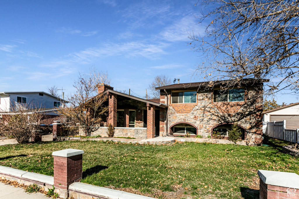 View of front of house with stone siding, brick siding, fence, and a front lawn