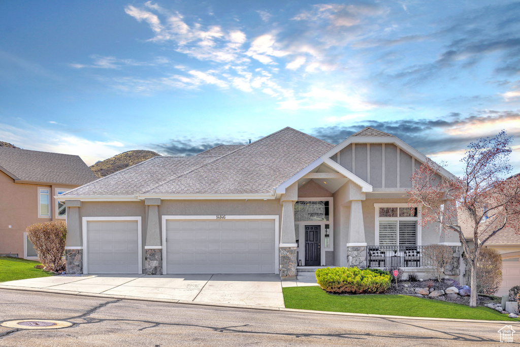 Craftsman-style house with an attached garage, stone siding, driveway, and stucco siding